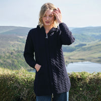 Woman wearing a navy knitted cardigan standing in a scenic outdoor setting with mountains and a lake.