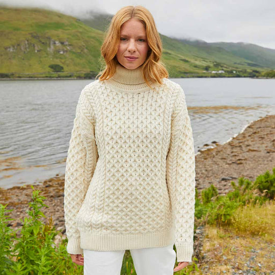 Woman wearing a cream Women's Signature Fisherman Turtleneck Wool Sweater standing by a lake with mountains in the background
