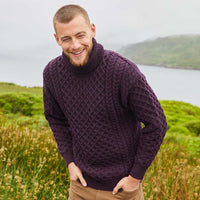 Man wearing a damson Men's Signature Fisherman Turtleneck Wool Sweater standing in a scenic outdoor setting with a lake and mountains.