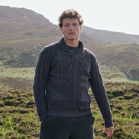Image featuring the Men's Classic V-Neck One Button Aran Sweater in cormorant blue, crafted with authentic Irish Aran cable knit patterns and a signature one-button shawl collar, showcasing timeless Irish craftsmanship in a scenic countryside setting.