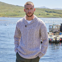 Man wearing an oatmeal colored Aran sweater by a body of water with mountains in the background