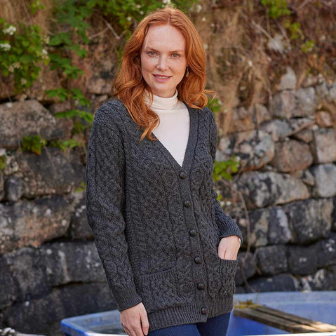 Woman wearing a charcoal Women's Classic Aran Boyfriend Button-Front Cardigan standing in front of a stone wall.