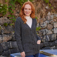 Woman wearing a charcoal Women's Classic Aran Boyfriend Button-Front Cardigan standing in front of a stone wall.
