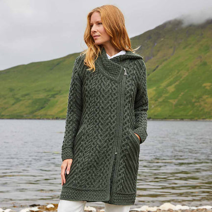 Woman wearing a green Women's Heritage Aran Hooded Zipper Coat standing by a lake with mountains in the background