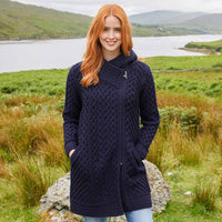 Woman wearing a navy blue Women's Heritage Aran Hooded Zipper Coat standing in a scenic outdoor setting with a lake and mountains.