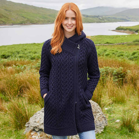 Woman wearing a navy blue Women's Heritage Aran Hooded Zipper Coat standing in a scenic outdoor setting with a lake and mountains.