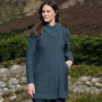 Woman wearing a peacock knitted coat standing outdoors with a natural background