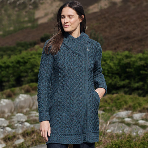Woman wearing a peacock knitted coat standing outdoors with a natural background