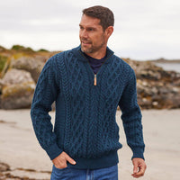 Man wearing a navy blue Aran sweater on a beach with a rocky background
