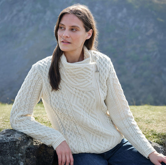 Woman wearing a cream Women's Signature Aran Wool Zipper Cardigan sitting outdoors with mountains in the background