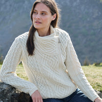 Woman wearing a cream knitted sweater sitting outdoors with mountains in the background