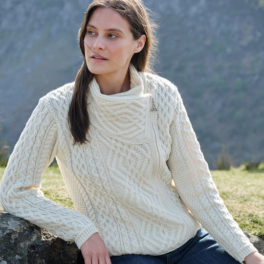 Woman wearing a cream knitted sweater sitting outdoors with mountains in the background
