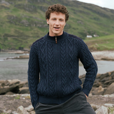 Image featuring the Men's Fisherman Full Zip Cardigan in Blackwatch, crafted with authentic Irish fisherman cable knit patterns, a full-zip fastening, and a ribbed stand collar, showcasing timeless Irish craftsmanship in a scenic coastal landscape.