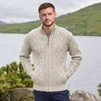 Image featuring the Men's Fisherman Full Zip Cardigan in oatmeal, crafted with authentic Irish fisherman cable knit patterns, a full-zip fastening, and a ribbed stand collar, showcasing timeless Irish craftsmanship against a scenic lakeside landscape inspired by Ireland's rugged countryside.