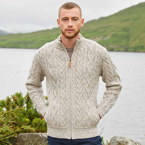 Man wearing an oatmeal Men's Fisherman Full-Zip Aran Cardigan standing by a lake with mountains in the background