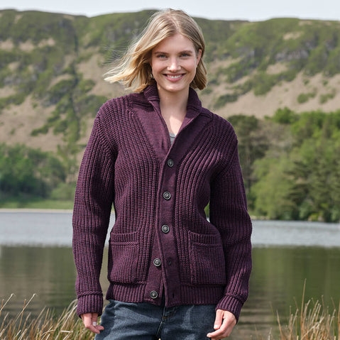 Woman wearing a purple Aran cardigan standing by a lake with green hills in the background