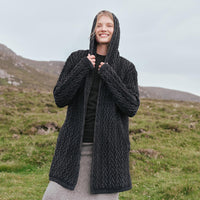 Image featuring the Women's Signature Hooded Aran Waterfall Cardigan in charcoal, crafted with authentic Irish Aran cable knit patterns, a flowing waterfall silhouette, and a comfortable hood, showcasing timeless Irish craftsmanship in a scenic countryside setting.