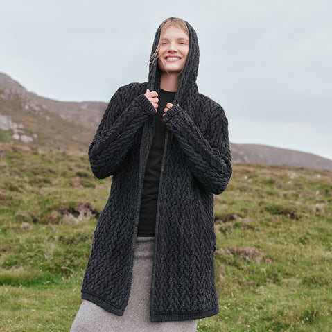 Image featuring the Women's Signature Hooded Aran Waterfall Cardigan in charcoal, crafted with authentic Irish Aran cable knit patterns, a flowing waterfall silhouette, and a comfortable hood, showcasing timeless Irish craftsmanship in a scenic countryside setting.