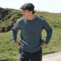 Men's Fisherman Lightweight Crew Neck Heritage Sweater in Lichen, featuring traditional Irish cable knit craftsmanship and heritage-inspired stitching, styled outdoors in the rugged Irish countryside with a classic Irish flat cap.