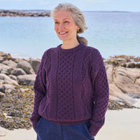 Woman wearing a damsonWomens Fisherman Lightweight Crew Neck Heritage Sweater standing on a beach with ocean in the background