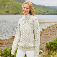 Woman wearing a beige Womens Fisherman Lightweight Crew Neck Heritage Sweater by a lake with mountains in the background