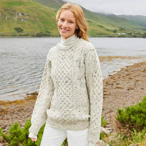 Woman wearing a beige Womens Fisherman Lightweight Crew Neck Heritage Sweater by a lake with mountains in the background