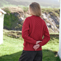 Back view of the Women's Fisherman Lightweight Crew Neck Heritage Sweater in Cranberry Red, showcasing intricate traditional Irish cable knit stitching and authentic heritage craftsmanship against a scenic Irish coastal backdrop.