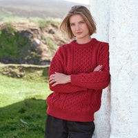 Women's Fisherman Lightweight Crew Neck Heritage Sweater in Cranberry Red, showcasing traditional Irish cable knit craftsmanship and heritage-inspired stitching, styled outdoors against the scenic Irish countryside.