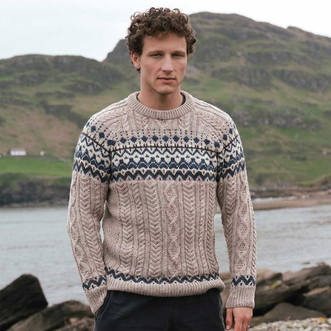 Image featuring the Men's Fair Isle Cable Knit Sweater in oatmeal, crafted with authentic Irish cable knit textures and traditional Fair Isle motifs in blue and cream, showcasing timeless heritage knitwear against a rugged coastal landscape.