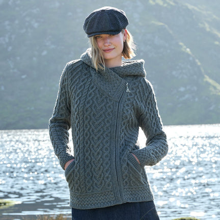 Woman wearing a gray knitted jacket with a hood by a body of water.