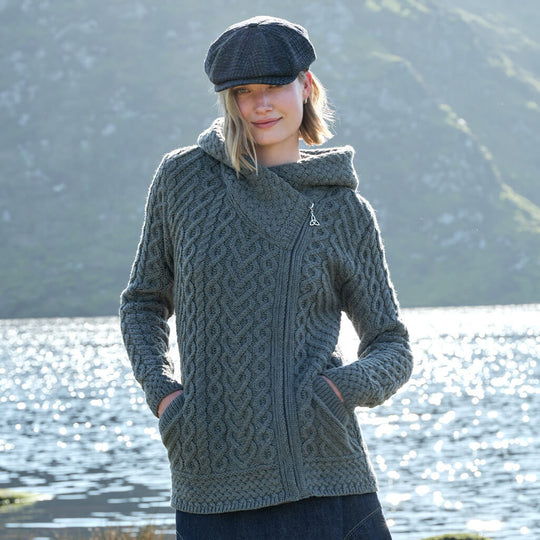 Woman wearing a gray knitted jacket with a hood by a body of water.