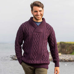 Man wearing a damson Men's Shawl Collar Heritage Aran Sweater by a body of water