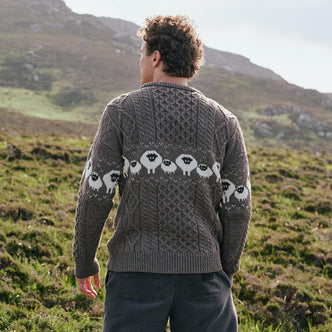 Image featuring the Traditional Sheep Aran Sweater in brown, crafted with authentic Irish Aran knit patterns and iconic sheep motifs, showcasing the detailed heritage-inspired design against Ireland's scenic countryside.