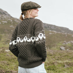 Image featuring the Traditional Sheep Aran Sweater in brown, crafted with authentic Irish Aran knit patterns and iconic sheep motifs across the back and sleeves, showcasing heritage-inspired Irish knitwear against a scenic countryside backdrop.