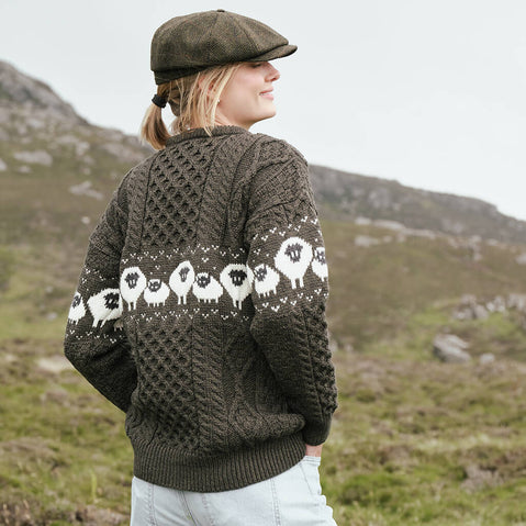 Image featuring the Traditional Sheep Aran Sweater in brown, crafted with authentic Irish Aran knit patterns and iconic sheep motifs across the back and sleeves, showcasing heritage-inspired Irish knitwear against a scenic countryside backdrop.