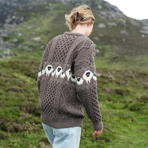 Image featuring the Traditional Sheep Aran Sweater in charcoal, crafted with authentic Irish Aran cable knit patterns and a signature sheep design inspired by Ireland’s farming heritage, showcasing traditional craftsmanship from a rear view against a scenic countryside backdrop.