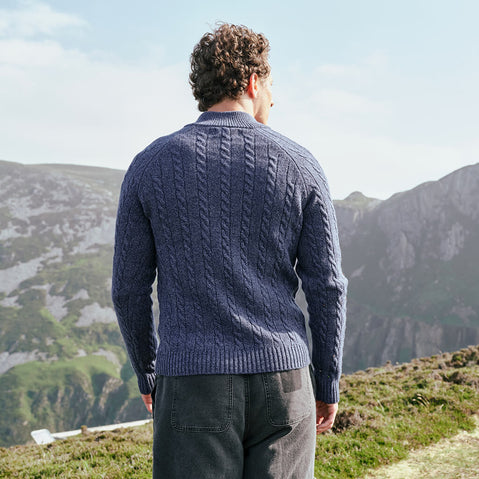 Image featuring the Men's Traditional Half Zip Cable Knit Sweater in indigo, crafted with authentic Irish cable knit patterns and a practical half-zip neckline, showcasing the detailed knit design against Ireland's rugged mountain scenery.