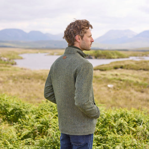 A man standing outdoors wearing a blue Donegal herringbone zipper jacket with long sleeves, paired with jeans.