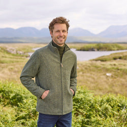 A man standing outdoors wearing a blue Donegal herringbone zipper jacket with long sleeves, paired with jeans.