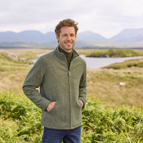 A man standing outdoors wearing a blue Donegal herringbone zipper jacket with long sleeves, paired with jeans.