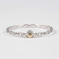 A Claddagh bracelet with a Celtic plaited design, featuring a gold heart at the center, crafted in silver.