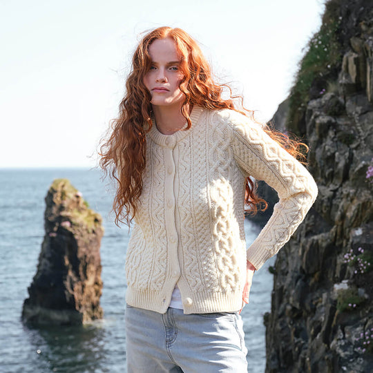 Image featuring the Women's Button Front Short Aran Sweater Cardigan in natural cream, crafted with authentic Irish Aran cable knit patterns and a classic button-front design, inspired by Ireland's rich knitting heritage and coastal landscapes.