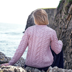 Image featuring the Women's V-Neck Cable Knit Aran Sweater in pink, crafted with authentic Irish cable knit patterns and a timeless V-neck silhouette, showcasing traditional Aran craftsmanship in a scenic coastal setting.