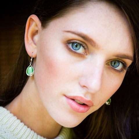 Green cat’s eye Claddagh drop earrings in a silver setting, worn with a cream knit traditional aran sweater