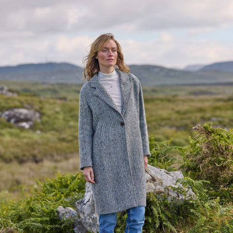 A woman standing outdoors wearing a gray herringbone tweed coat with a classic design.