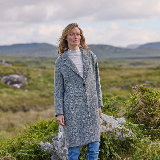 A woman standing outdoors wearing a gray herringbone tweed coat with a classic design.