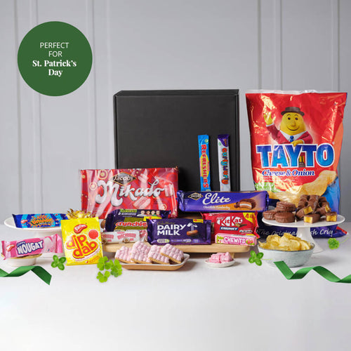 Assorted candy and snacks on a white surface with a gray background, featuring a 'Tayto' bag and text indicating suitability for St. Patrick's Day.