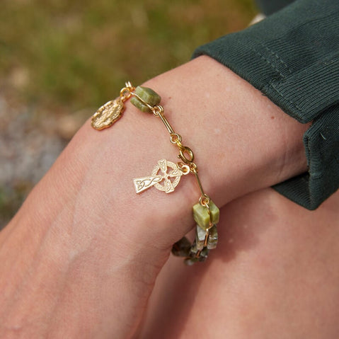 Connemara marble rosary bracelet with gold-tone chain, featuring a Celtic Cross charm and oval saint medal, worn on the wrist outdoors.