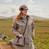A multicolored tweed handbag with a black leather handle and metal twist clasp, sitting on a mossy surface.