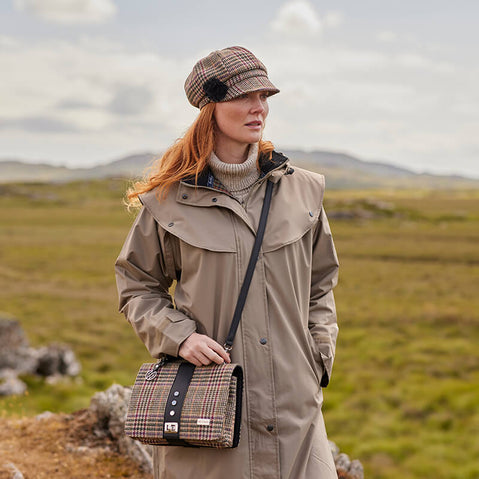A multicolored tweed handbag with a black leather handle and metal twist clasp, sitting on a mossy surface.